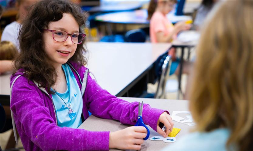 A girl wearing a purple jacket smiles while talking to her classmate